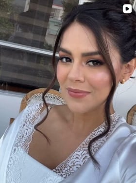 Mujer con recogido de mechones sueltos, ojos definidos, rubor y labios rosados, con una bata de encaje blanca