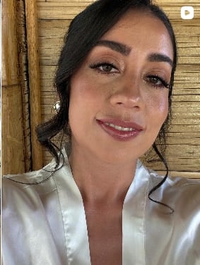 Mujer con recogido de ondas sueltas, ojos delineados y labios rosados, con una bata de satén blanca frente a una pared de bambú