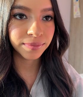 Maquillaje suave para quince años: joven de cabello largo ondulado y oscuro con piel luminosa, rubor rosado y labios rosados